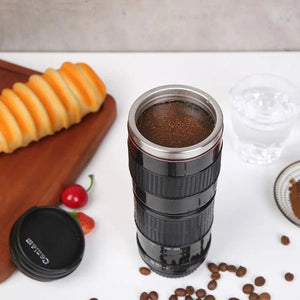 A black travel mug designed to resemble a camera lens is featured in a four-panel image demonstrating its use. The mug is shown being filled with hot water from a kettle and then appearing full of coffee. Coffee beans and pastries are present in some panels.kitchen supply store, Kitchen items, coffee mug travel essentials, travel accessories