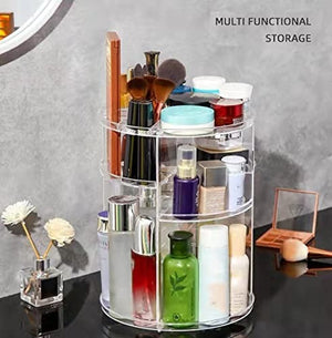 A clear, three-tiered Yibang 360 Degree Rotating Cosmetic Makeup Organizer is filled with various makeup brushes, palettes, and skincare bottles. The organizer sits on a black surface, with a small vase of artificial flowers to the left and a compact mirror with a brush to the right. Text at the top reads MULTI FUNCTIONAL STORAGE.Yibang rotating organizer, makeup storage, cosmetic organizer, 360 degree storage, multi-functional storage.