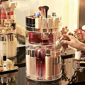 A clear, multi-tiered cosmetic organizer rotates on a vanity table. 1  The organizer holds various makeup items, including lipsticks, brushes, jars, and bottles of skincare products. A hand reaches in to select a perfume bottle from one of the rotating shelves. Rotating makeup organizer, adjustable cosmetic storage, vanity organizer, makeup display, skincare organizer. Ā