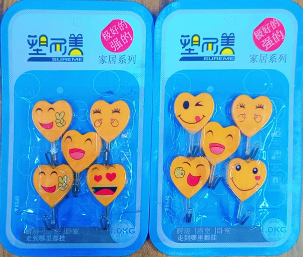 5 packs of yellow heart-shaped self-adhesive hooks with cute cartoon faces are displayed. Each pack contains five plastic hooks designed for easy, no-drill wall mounting. The packaging indicates they are "strong" and suitable for home use, likely for organizing lightweight items. Keywords: heart hooks, sticky hooks, cute hooks, wall organization, self-adhesive.