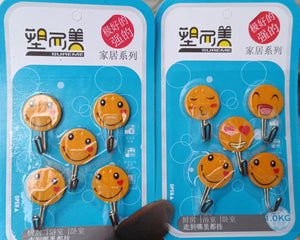 5 packs of round, yellow self-adhesive hooks with various smiling emoji faces are shown. Each pack contains five plastic hooks designed for easy, no-drill wall mounting. The packaging suggests they are "strong" and suitable for organizing lightweight items in homes. Keywords: emoji hooks, sticky hooks, cute hooks, wall organization, self-adhesive.