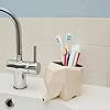 A bathroom sink with a chrome faucet is complemented by a beige elephant-shaped holder, cleverly designed to store toothbrushes and toothpaste. The elephants trunk creatively serves as a water spout, while white tiles form the backdrop, echoing an Elephant Cutlery Holders whimsical charm.