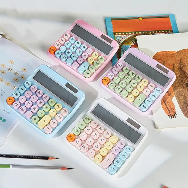 Four vintage typewriter-style solar calculators in pink, white, and light blue are arranged on a desk. Each calculator features round, pastel-colored keys and a digital display showing different numbers. A notebook with a cartoon illustration is visible in the background. solar calculators, vintage calculators, typewriter style, pastel keys, office supplies, desk accessories.