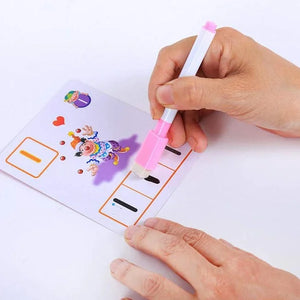 Two hands are shown interacting with a wipe-clean educational card. One hand holds the card, which features a picture of a clown and blank spaces with dotted lines. The other hand uses a pink and white marker to draw lines in the blank spaces. Wipe-clean card, educational activity, early learning, writing practice, pre-writing skills.