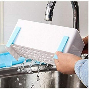 A pair of hands is shown rinsing a white plastic kitchen utensil holder with light blue accents under a running kitchen faucet. Water streams through the perforated base of the holder and into the stainless steel sink below.utensil holder, kitchen organiser, cutlery drainer, kitchen storage, dish drying rack, kitchen accessories, household items, kitchen items, KPS, drain rack, rinsing.