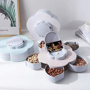 A light blue flower-shaped rotating tray with snacks in compartments and a phone holder in the center. Hands reach for snacks.snack tray, phone holder, rotating, serving dish.