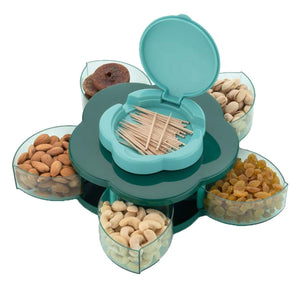 A green flower-shaped rotating tray with six clear compartments filled with nuts and dried fruit. A teal toothpick holder is in the center.snack tray, rotating, nuts, dried fruit, serving.