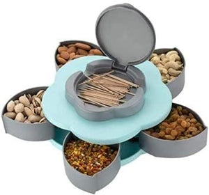 A Blue flower-shaped rotating tray with six clear compartments filled with nuts and dried fruit. A teal toothpick holder is in the center.