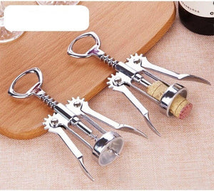Two silver wing corkscrews are placed on a wooden surface. One corkscrew has a cork inserted into it, ready to open a wine bottle. A wine bottle and a wine glass are partially visible in the background. Wine opener, corkscrew, bottle opener, barware, kitchen tool, home essential.