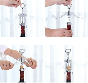 Two hands are using a silver wing corkscrew to open a bottle of red wine. The cork is partially extracted from the bottle. The background is blurred, suggesting a home setting. Wine opener, corkscrew, bottle opener, barware, kitchen tool, home essential.