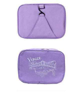 Two views of a light purple Venice travel cosmetic pouch are displayed against a white background. The top view shows the closed pouch with a hanging hook. The bottom view shows the front of the pouch, featuring the word "Venice" in cursive script and a white line drawing of a Venetian bridge and buildings. Venice Travel Cosmetic Pouch, makeup bag, travel organizer, toiletry bag, purple pouch.