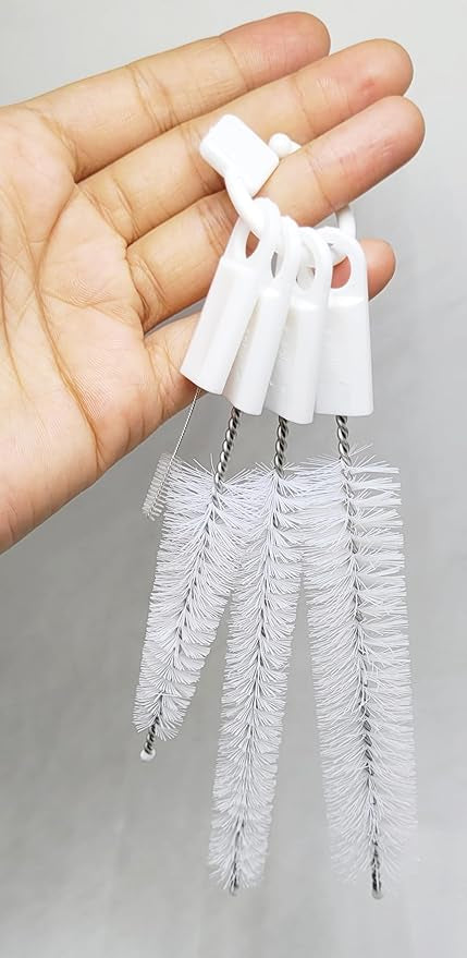 A hand holds a set of four white cleaning brushes on a ring.brush set, cleaning, handheld, kitchen.