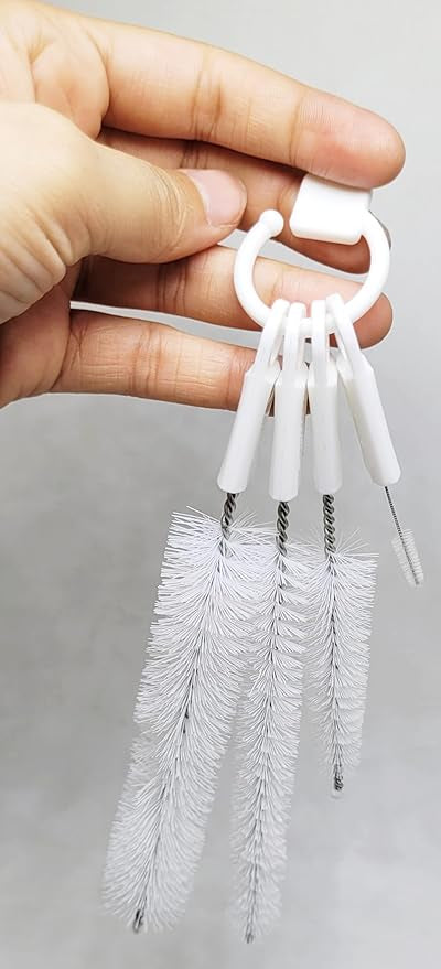 A hand holds a set of four white cleaning brushes connected by a white ring.brush set, cleaning tools, handheld.