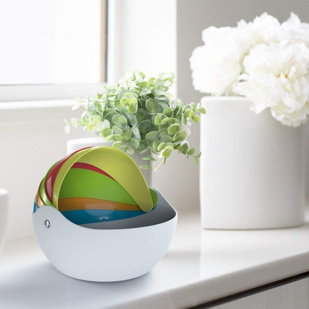  Colorful rainbow bowls in a white base sit on a counter with plants and flowers.rainbow bowls, serving bowls, kitchen decor, colorful.