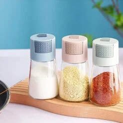 3 Glass Salt Dispenser is placed on a table. The seasoning dispenser shown are blue, pink, and grey color.