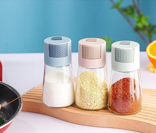 3 Glass Salt Dispenser is placed on a table. The seasoning dispenser shown are blue, pink, and grey color.