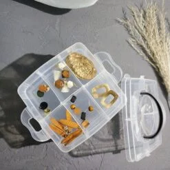 Transparent 6 grid storage box is placed on a table along with its lid beside it.