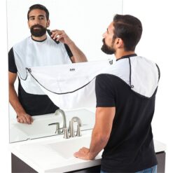 A guy in front of a mirror and wash basin is using shaving apron while shaving.