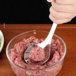 Cook is making meatballs using meatball making spoon.