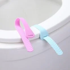 Blue color toilet seat cover lifter is installed on a toilet seat cover and a pink color toilet seat cover lifter is placed beside it.
