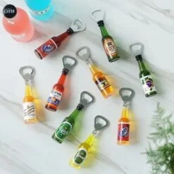 Mutiple and multicolor bottle shaped bottle opener is placed on a floor beside 2 soft drinks bottle
