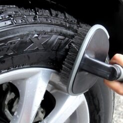 Car tyre is being cleaned with a black and grey color tyre scrubbing brush.