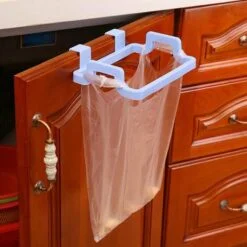 White color garbage bag hanger is mounted on a brown cabinet door and an orange color polythene is installed on it.