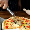 Woman is cutting pizza using stainless steel pizza cutter.