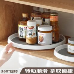 2 white and grey plastic rotating organizer are filled with different kitchen bottles. This plastic rotating organizer is kept under a cabinet.