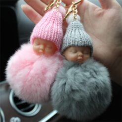 Cute doll key chain of pink and grey color held by a woman sitting in a car.