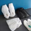 3 white color disposable shoe bags and 1 black color disposable shoe bag is presented besides a pair of white shoes.