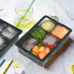 Black color silicone big ice cube tray is placed along with a juice glass and straw.
