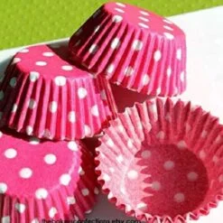 3 Pink color polka dot cup cake paper cups are kept on a table.