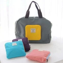 Grey color reusable grocery shopping bag is placed besides folded pink, blue, and purple color shopping bags.