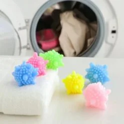 Multiple and multicolor laundry scrubbing balls are placed on a table in front of a washing machine.
