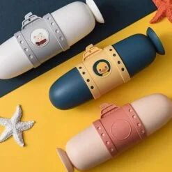 Submarine Shape plastic toothbrush case is presented in a grey, blue, and reddish color on a yellow and blue color table.