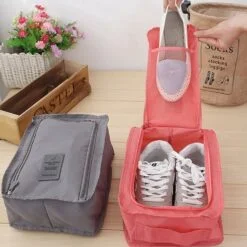 Grey color travelling shoe storage bag is placed on a left hand side. On the right hand side, woman is placing shoes in reddish color travelling shoe storage bag