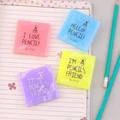 Printed eraser of pink, blue, yellow, and purple color are kept on a notebook besides 2 pencils