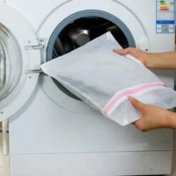 Nylon mesh laundry bag is being inserted in a washing machine.