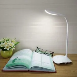 White color rechargeable touch led table lamp is throwing light on a book kept on a desk.