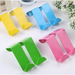 Yellow, blue, green, and pink color stainless steel over door hooks are placed on white color table besides flowers