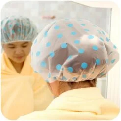 A woman in a bathrobe in front of a mirror is wearing a polka dot washable shower cap