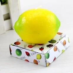 Lemon shaped candle is placed on a packet on a white color desk.