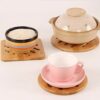 Square wooden placemat is used to place a bowl and two round wooden placemats are used to place cup saucer and a pot.
