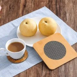 On a table, a hot tea cup is placed on a wooden placemat along with fruits in a plate.