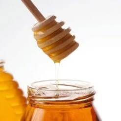 Mini wooden honey dipper is being used in a honey jar.