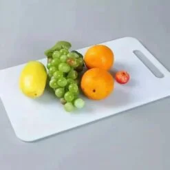 Mango, grapes, and oranges are kept on a white plastic chopping board.