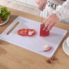 A girl is cutting red bell pepper on a white plastic chopping board.