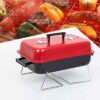 Black and red charcoal barbecue grill is placed on a white table.