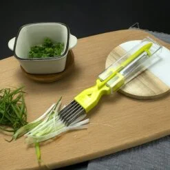 Yellow color 2 in 1 peeler and cutter is placed on a chopping board along with a white bowl filled with greens.